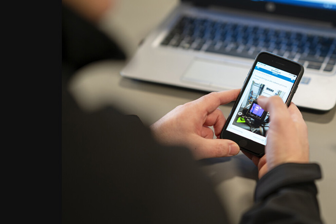 En person med en mobiltelefon i handen vid en dator