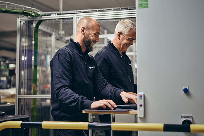 The image shows two technicians in an industrial environment