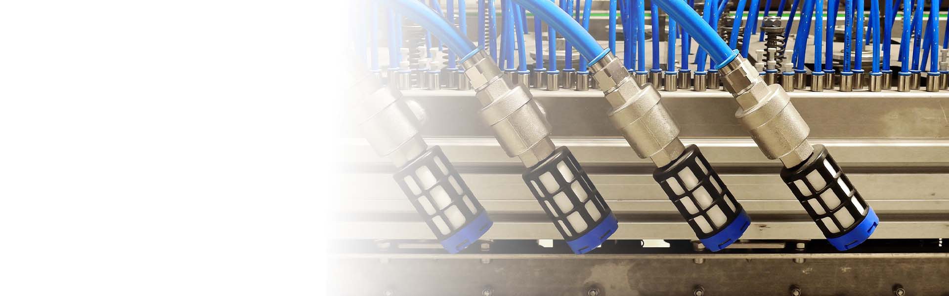 Närbild av industrikomponenter med blå slangar och metallkopplingar anslutna till ett hydrauliskt eller pneumatiskt system i en industriell anläggning.
