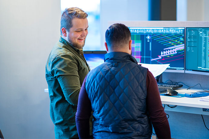 Två personer står vid datorer och diskuterar