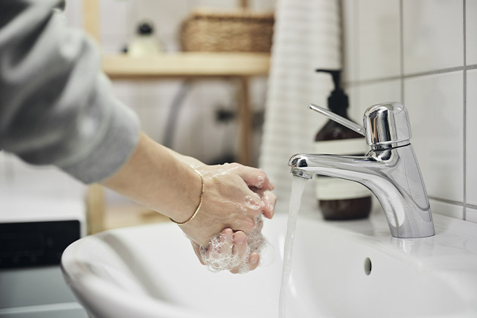 Bilden visar en person som tvättar sina händer i ett tvättställ
