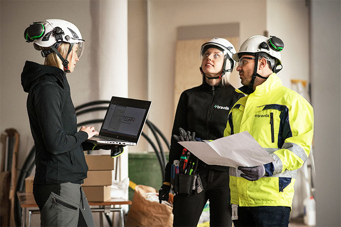 Tre personer från Bravida går igenom ritningar och information på en byggarbetsplats under ett installationsprojekt.