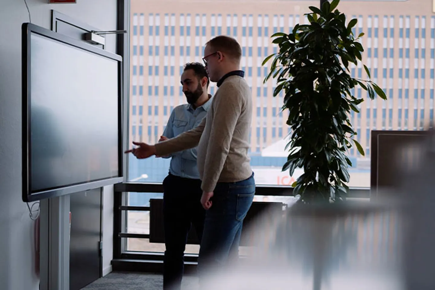 Två personer vid en digital skärm i kontorsmiljö under genomgång eller planering av ett projekt.