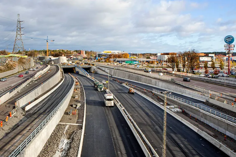 Väg- och tunnelprojekt under byggnation med flera körfält, arbetsfordon och omfattande infrastruktur.