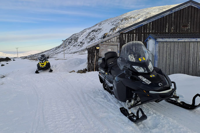 Bilden visar två skotrar vid ett hus i fjällvärlden 