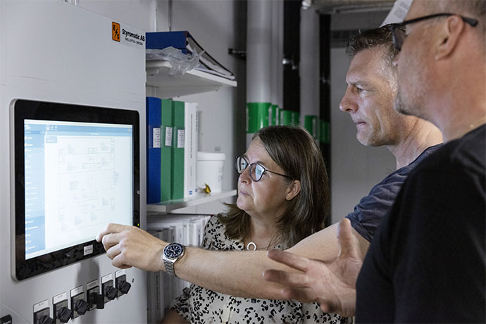 Three persons standing in front of a control panel